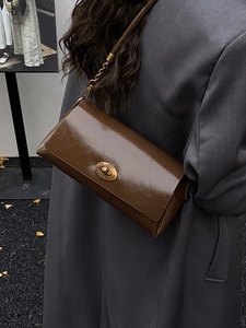 Sac bandoulière rétro en cuir marron brillant avec boucle dorée sur une veste grise