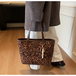 Detail of leopard print tote bag with metallic logo plate and vintage bead charm
