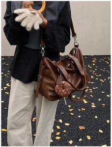 Detail of dark brown leather tote bag with plush doughnut charm and adjustable strap