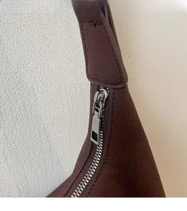 Detail of silver metal zipper and brown textured leather on stylish crossbody bag