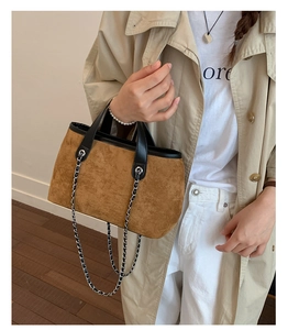 Brown suede bucket bag with chain strap and black handles styled on a beige trench coat