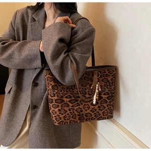 Detail of leopard print tote bag with brown leather straps and beaded tassel charm accessory