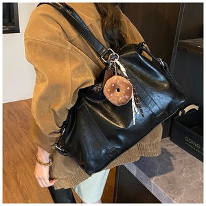 Detail of black faux leather tote bag with brown donut plush charm and long strap
