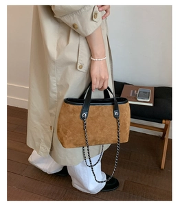 Close-up of vintage brown suede bucket bag featuring black leather handles and silver chain
