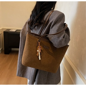 Detail of dark brown matte tote bag featuring beaded charm and smooth suede texture