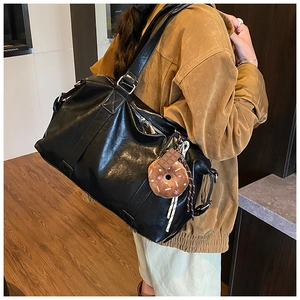 Detail of black leather tote bag with donut charms and shoulder straps worn by a model