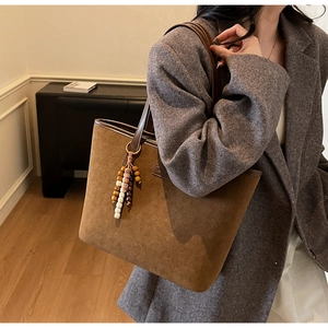 Detail of a large brown suede tote bag featuring bohemian beaded charm and leather straps