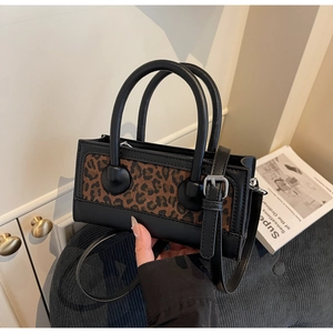 Detailed view of women's leopard print handbag with black leather handles and shoulder strap