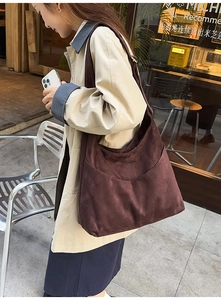 Vue détaillée d'un grand sac hobo en daim marron foncé porté avec un trench-coat décontracté
