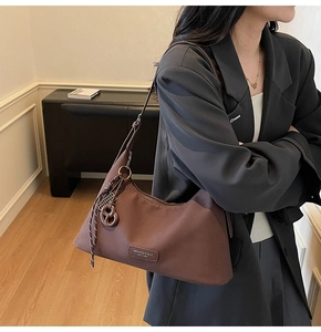 Detail of dark brown matte leather crossbody bag with logo patch and woven tassel accent