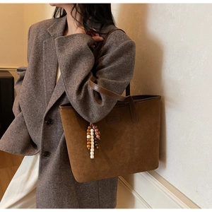 Detail of matte suede tote bag with wooden bead charm and brown leather handles