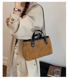 Close-up of brown suede bucket bag with black leather handles and silver chain strap