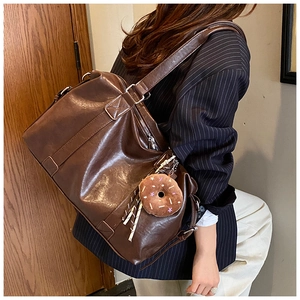 Close-up of a large brown leather tote bag with a plush donut charm on a model's shoulder