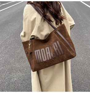 Macro shot of brown suede tote bag with MOACRI stitching and decorative elephant charm