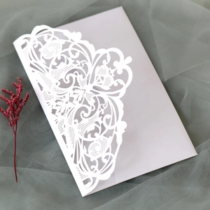 Detailed laser-cut lace floral pattern on white wedding invitation suite with dried flowers