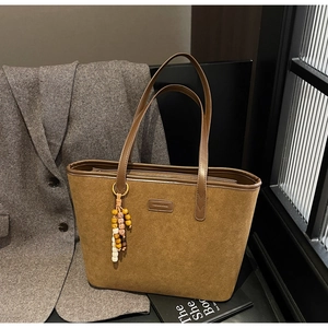 Detail view of brown suede tote bag featuring a leather logo tag and colorful wooden beads