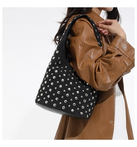 Dettaglio della borsa tote nera con borchie argentate indossata con cappotto di pelle