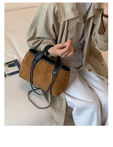 Detail of brown suede bucket bag with black leather trim and silver metal chain strap