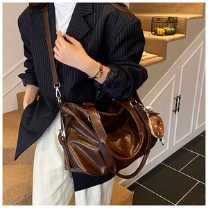 Detail of dark brown faux leather tote with plush charm on a model's shoulder