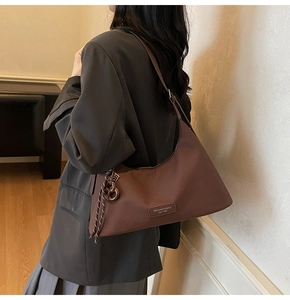 Detail of coffee brown crescent crossbody bag with branded tag and woven rope charm