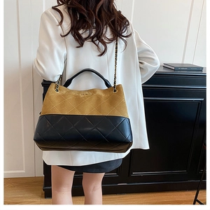 Detail view of quilted dual-tone beige and black bucket bag with gold chain strap