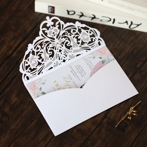Detail of laser-cut white lace wedding invitation with floral insert on wood background