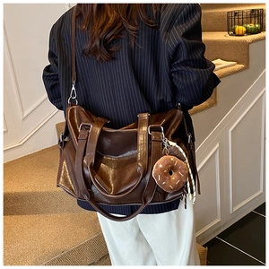 Detail of dark brown faux leather tote bag with donut charm and checkered scarf accessory