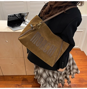 Detail of a large brown suede tote bag featuring embossed logo and a decorative bow