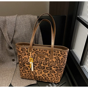 Detail of leopard print tote bag featuring brown leather handles and wooden bead charm