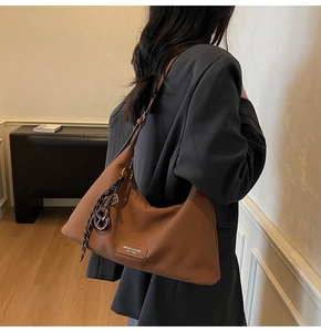Detail of brown lychee grain leather crossbody bag with woven knot charm on a model