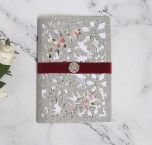 Detail of silver glitter laser-cut snowflake wedding invitation with red ribbon and rhinestone