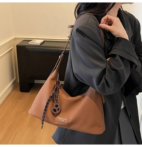 Detail of a brown leather crescent shoulder bag with silk scarf charm and logo label
