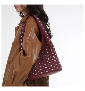 Dettaglio della borsa hobo bordeaux con borchie argentate indossata su un cappotto marrone