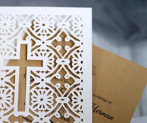 Macro detail of laser-cut floral patterns and cross design on white wedding invitation