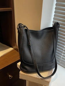 Classic black litchi pattern leather bucket bag placed on vintage books in warm light