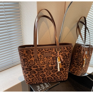 Detail of leopard print tote bag featuring brown leather straps and beaded charm accessory