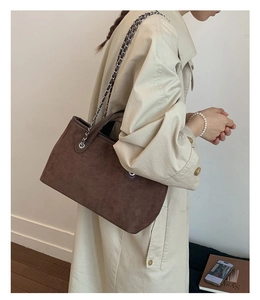 Detail of dark brown suede tote bag featuring metallic chain strap and silver eyelets