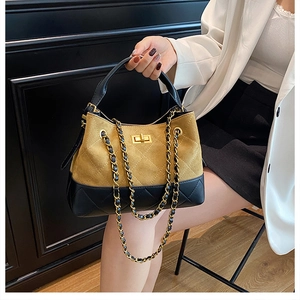 Close-up of mustard yellow and black patchwork handbag with gold metal twist lock
