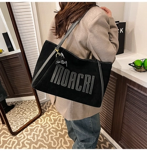 Detail of black suede tote bag with MOACRI embroidery and metal bow charm accessory