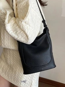 Fashionable black lychee grain leather bucket bag styled on a white cable knit sweater