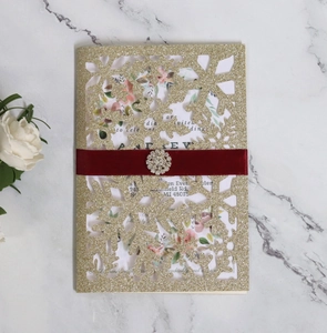 Detail of laser-cut gold glitter snowflake wedding invitation with red silk ribbon