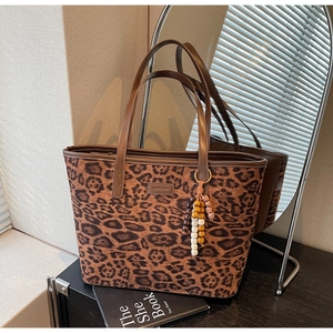 Detail of leopard print tote bag with brown leather straps and wooden bead charm accessory
