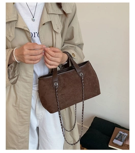 Close-up of dark brown suede bucket bag featuring silver chain and leather handle texture