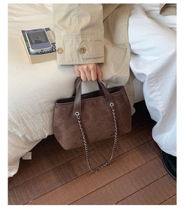 Detail of dark brown suede bucket bag with leather handle and metal chain strap