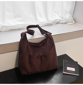 Détail d'un grand sac hobo en daim marron foncé avec bandoulière large et poche courbée