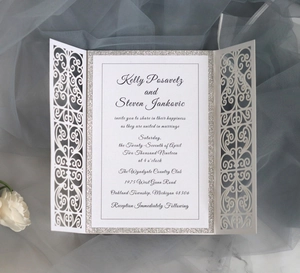 Macro detail of white laser-cut wedding invitation with silver glitter card and floral accent