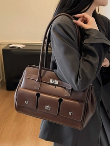 Brown vintage faux leather tote bag with silver flip locks worn by a model in black suit
