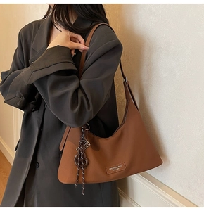 Detail of brown leather hobo bag with woven cord charm and logo patch on a model