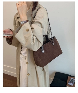 Detail of dark brown suede shoulder bag with silver chain strap on a trench coat