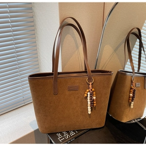 Close-up of brown suede tote bag with zipper closure and decorative wooden bead tassel